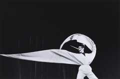 black background with a figure dressed in white in the foreground. One arm is curved over their head and the second poitning away from their body.